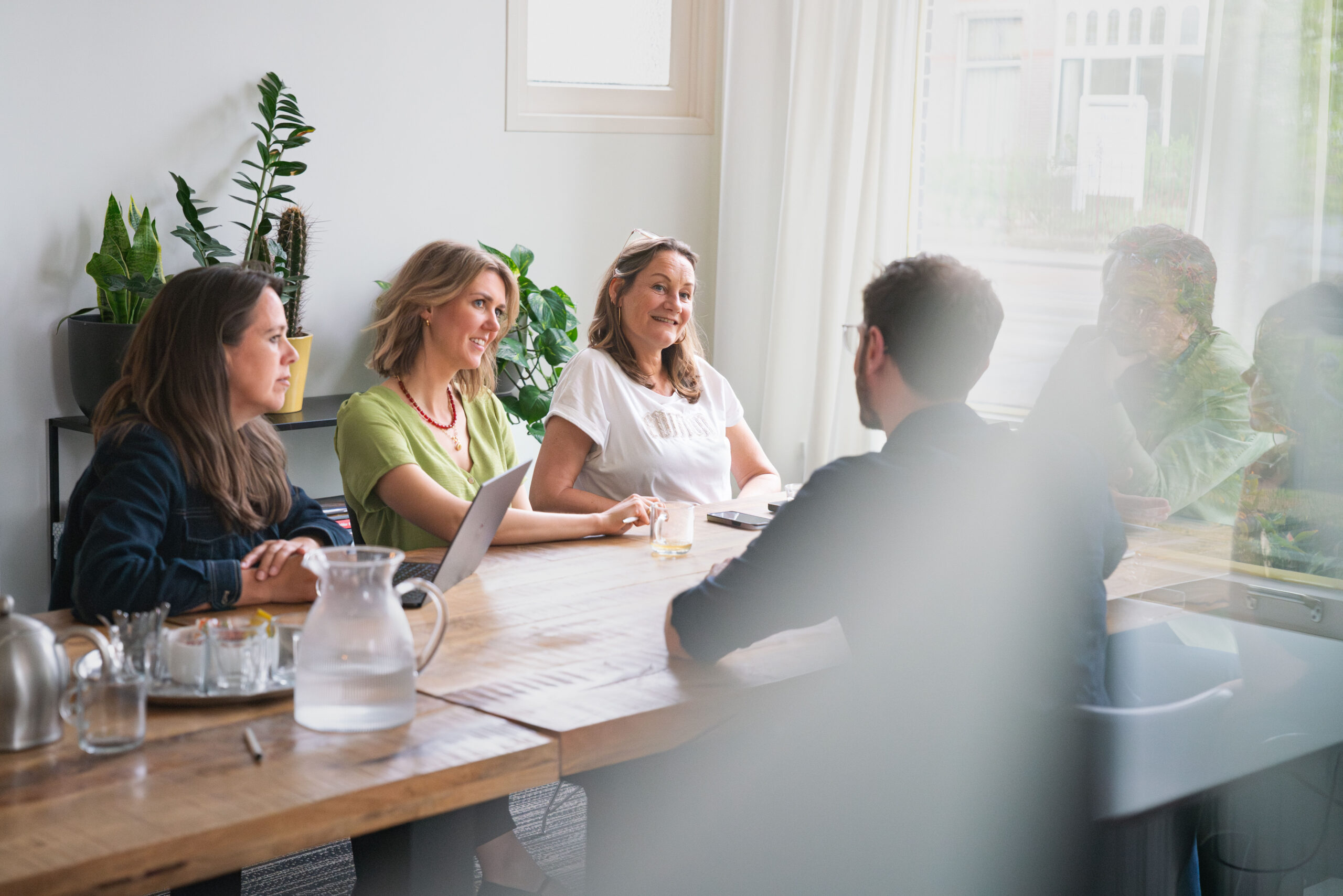Collega’s zitten in gesprek aan een houten tafel in een lichte vergaderruimte.