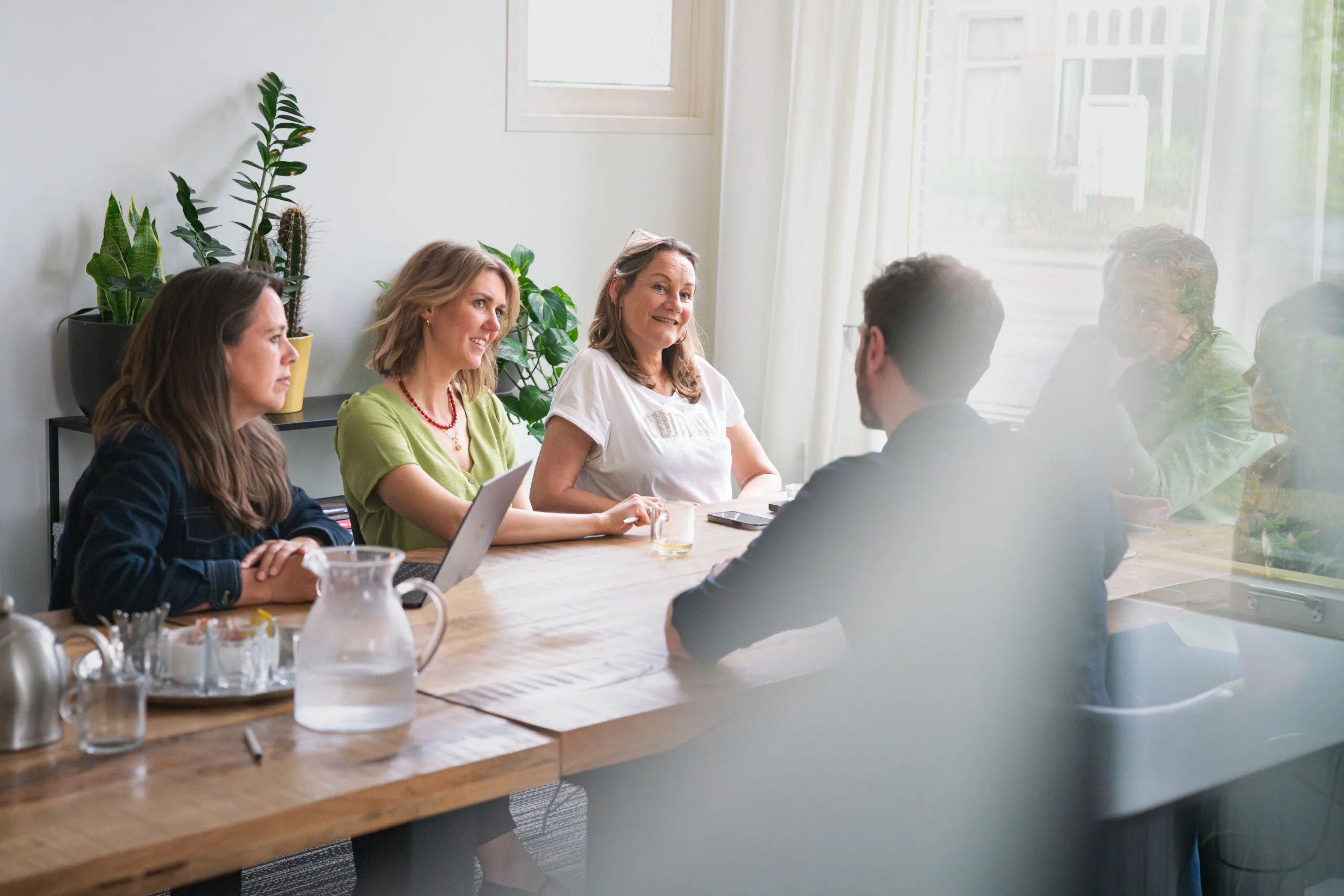 Collega’s zitten in gesprek aan een houten tafel in een lichte vergaderruimte.