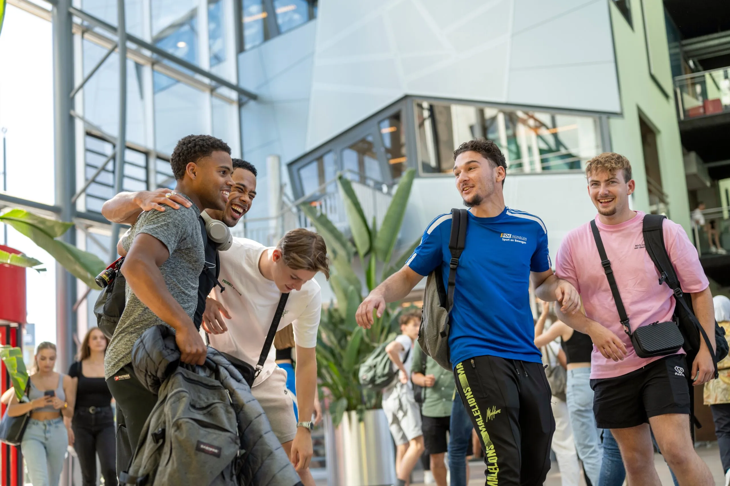 Groep lachende studenten loopt samen door de moderne hal van ROC Nijmegen.