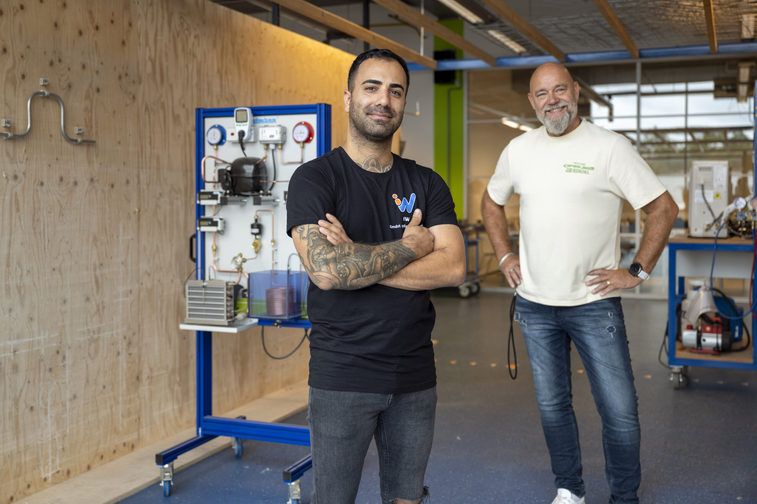 Docenten in een praktijkruimte voor techniekonderwijs, met gereedschap en opstellingen achter hen.