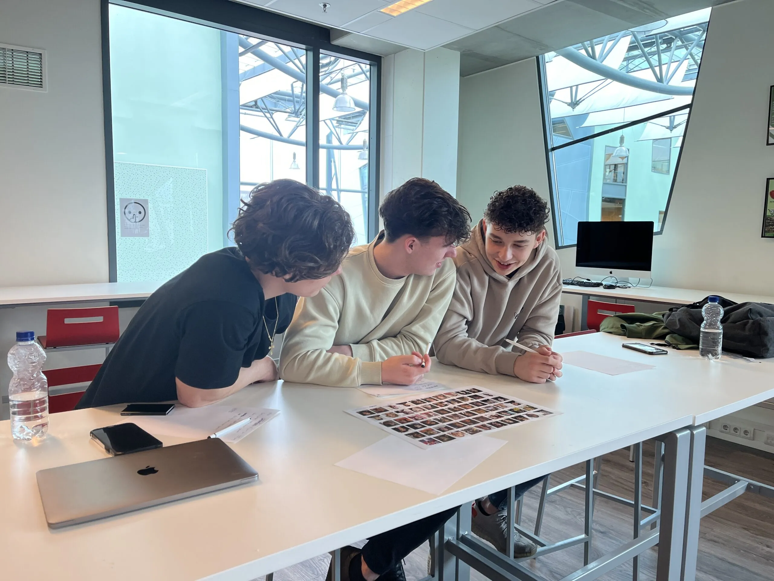 Jongeren werken samen lachend boven een vel met foto’s.