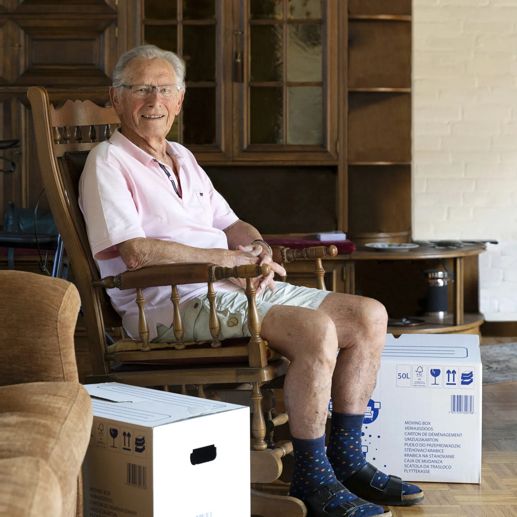 Oudere man zit in zijn schommelstoel tussen de verhuisdozen.