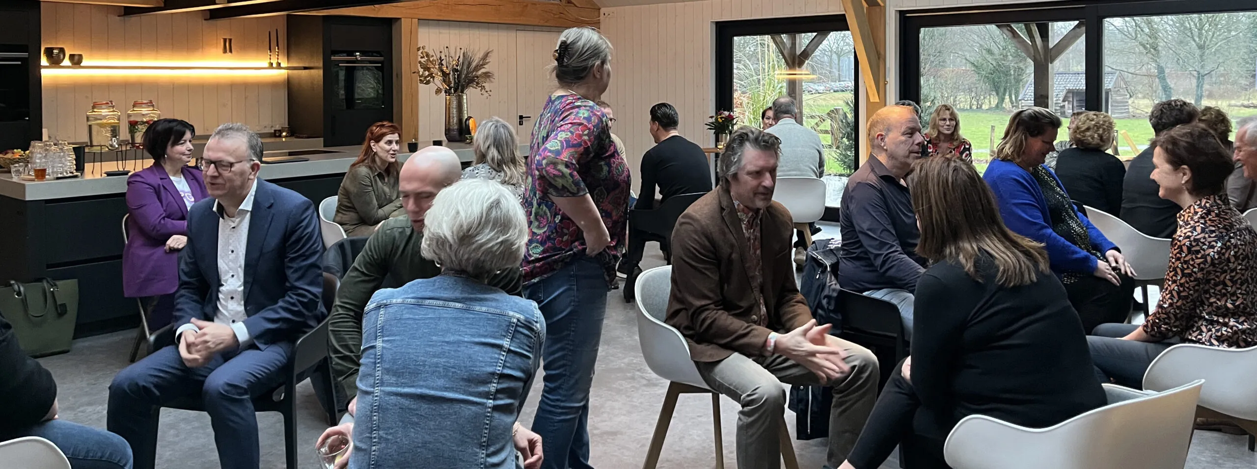 Deelnemers in gesprek in kleine groepjes tijdens een werksessie in een lichte ruimte met grote ramen