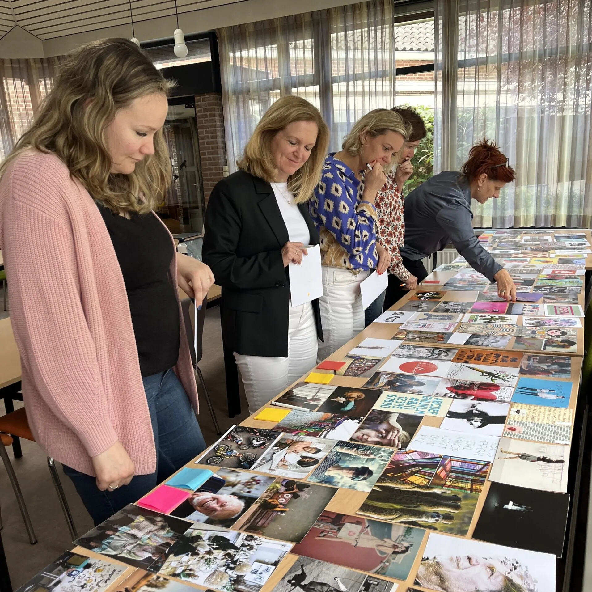 Deelnemers selecteren en bespreken afbeeldingen op een tafel tijdens een creatieve werksessie.